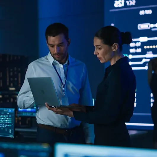 Two cybersecurity managers discussing strategy in office referencing information on laptop